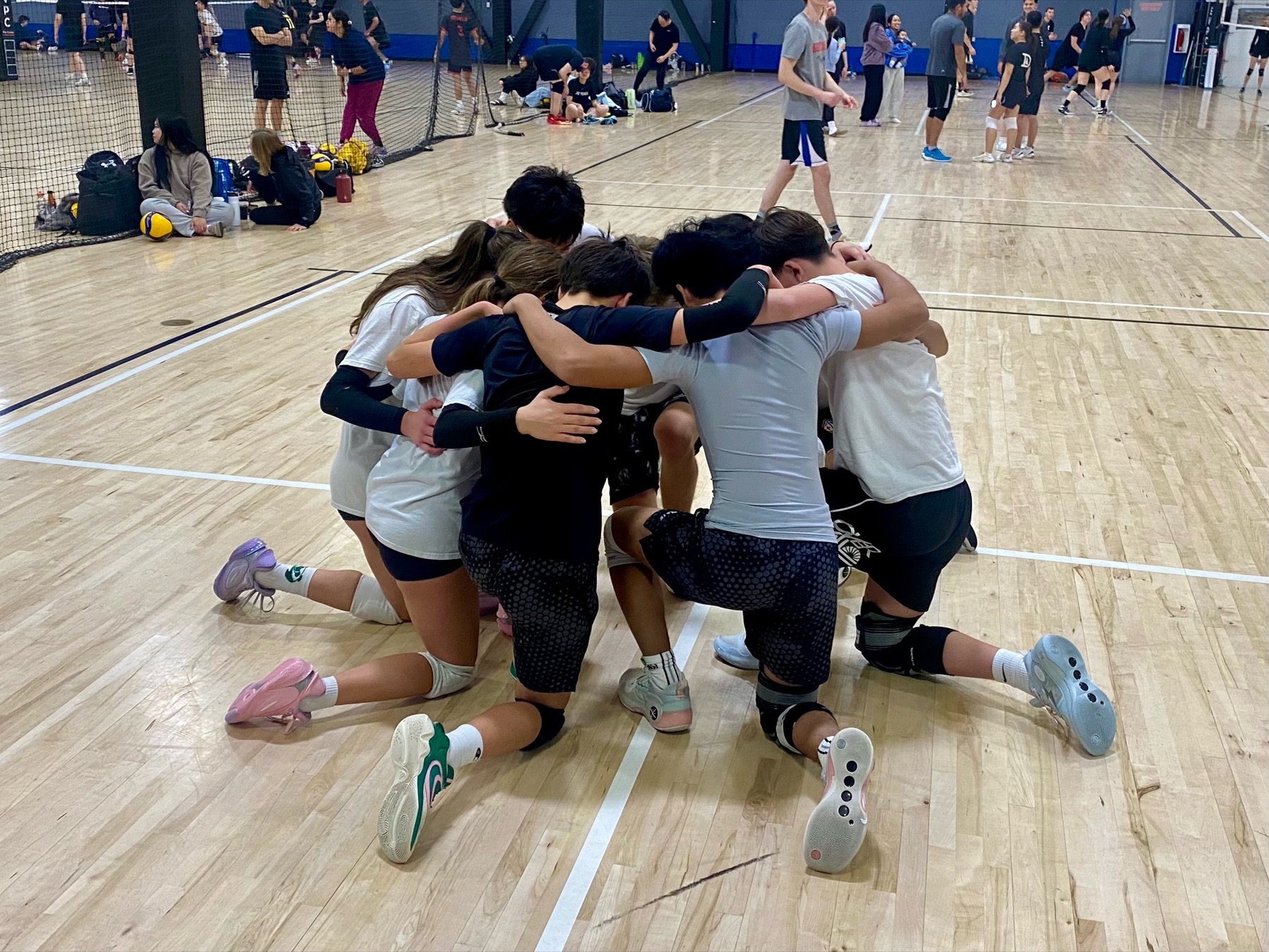 A volleyball team kneeling in a tight huddle on the court, arms around each other