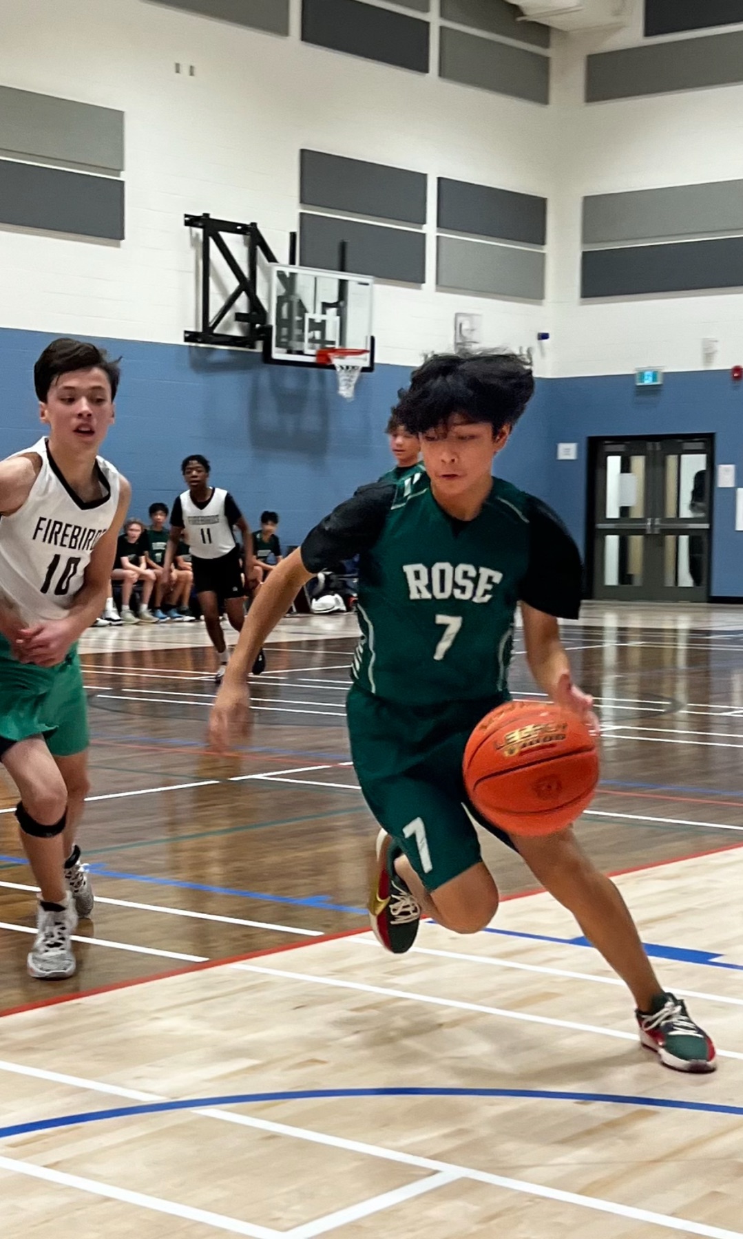 Basketball player number 7 in a green Rose jersey driving hard to the basket with a defender chasing