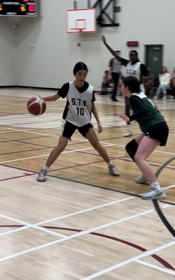 Girls basketball player number 10 in white handling the ball against a defender in green